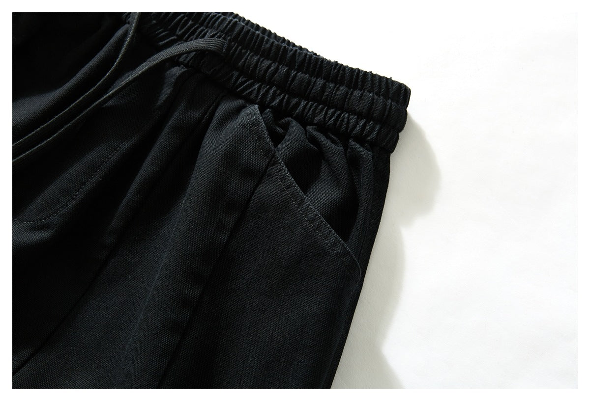 Close-up of black trousers showing the gathered elastic waistband and angled pocket opening.