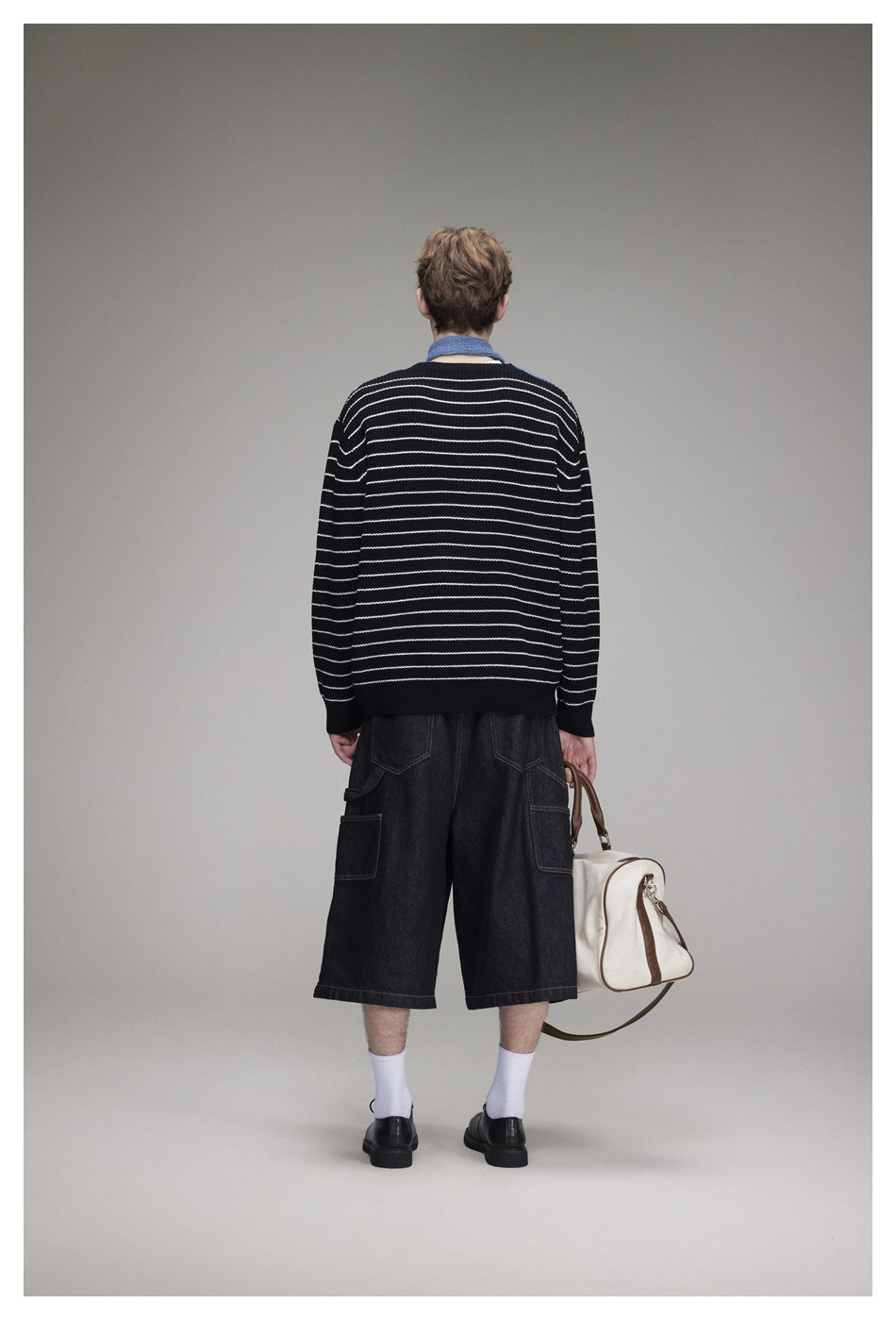 Rear view of a person wearing a black sweater with thin white horizontal stripes and dark shorts.