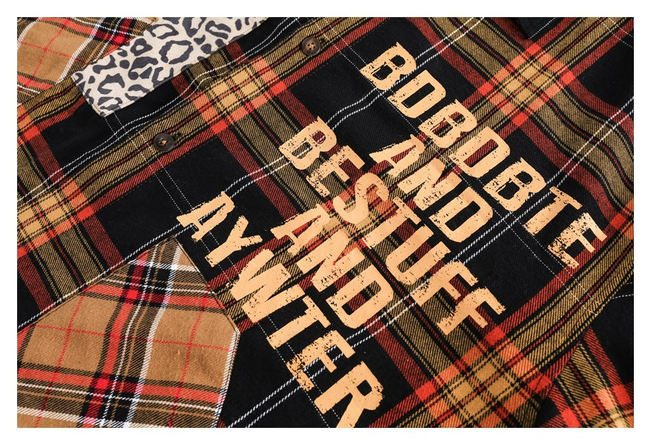 Close-up of a black, red and tan plaid shirt with distressed peach lettering and contrasting patterned fabric patches.