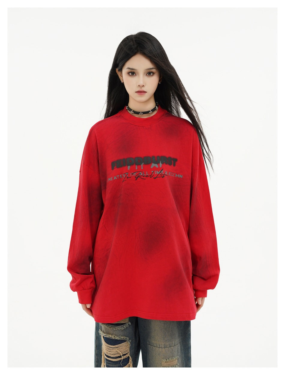 Model wearing an oversized red long-sleeve top with dark spots and chest print, styled with distressed jeans, front view