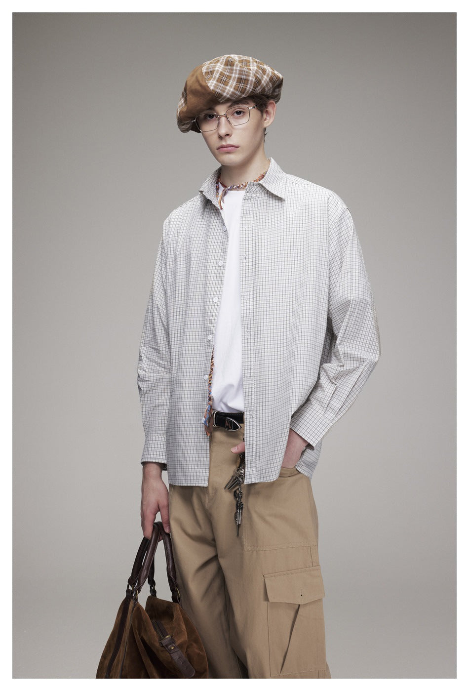 Model in an open check shirt over a white tee, with a plaid beret, khaki cargo pants and a brown suede bag