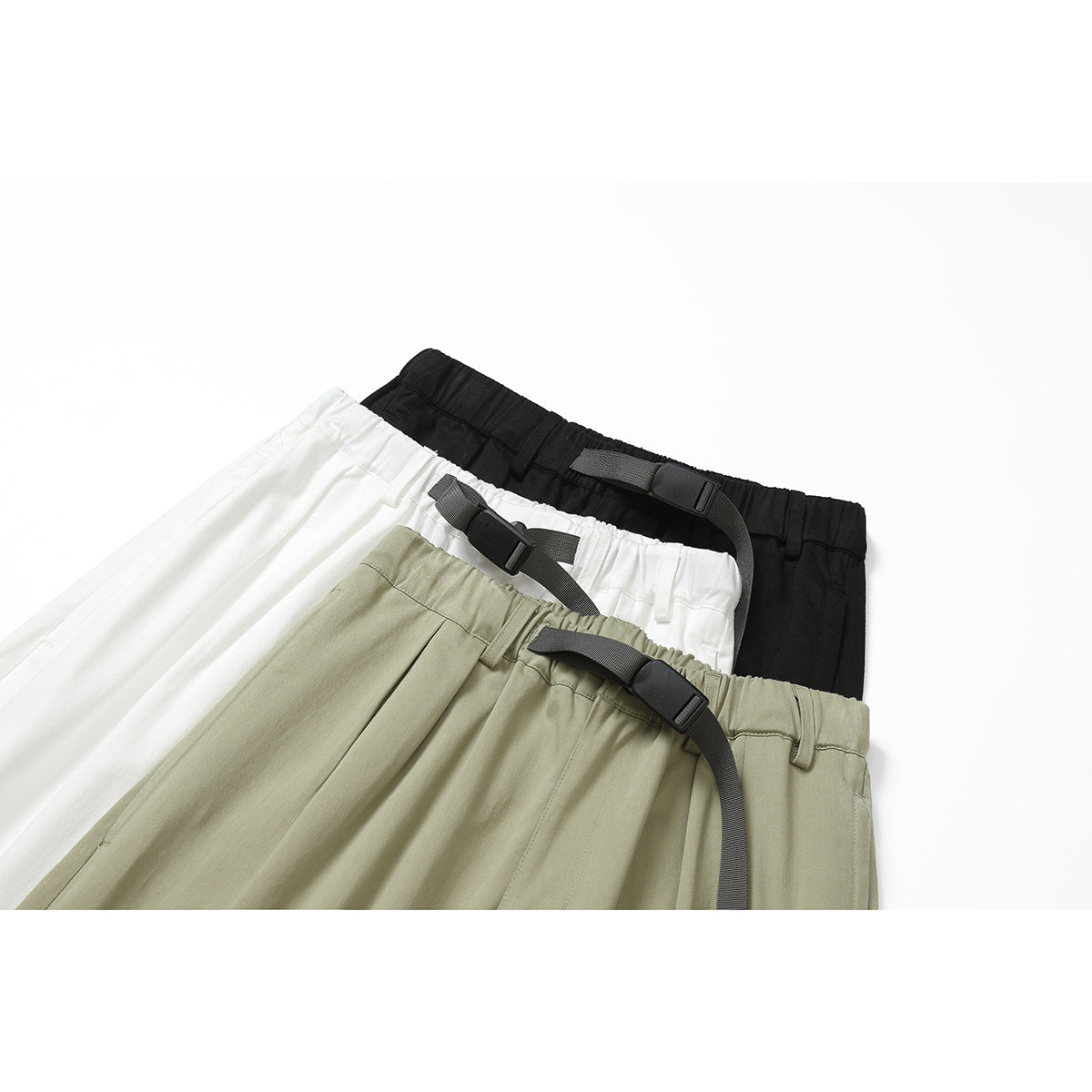 Close-up of black, white, and light olive trousers with elastic waistbands and gray webbing belts.