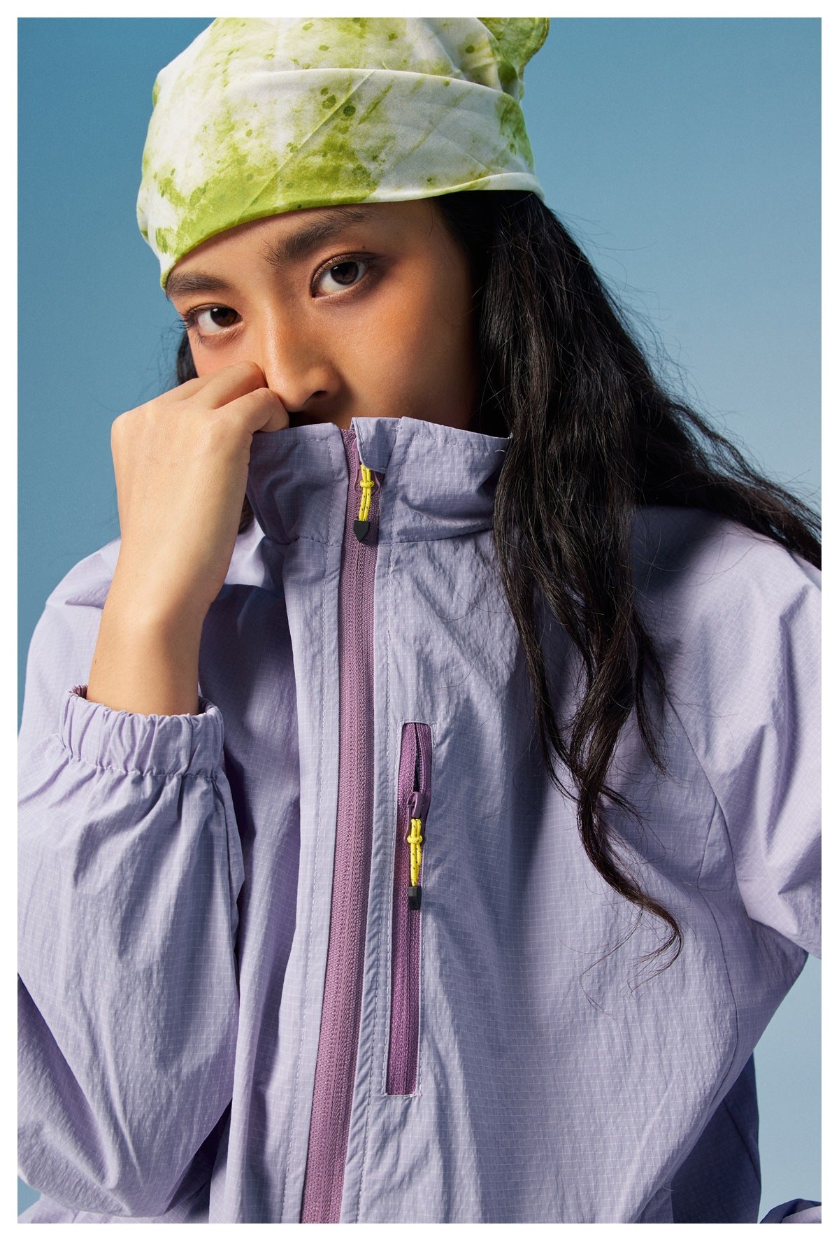 Close-up of a pale lavender jacket showing its high collar, front zipper, chest pocket zipper, and gathered cuff.
