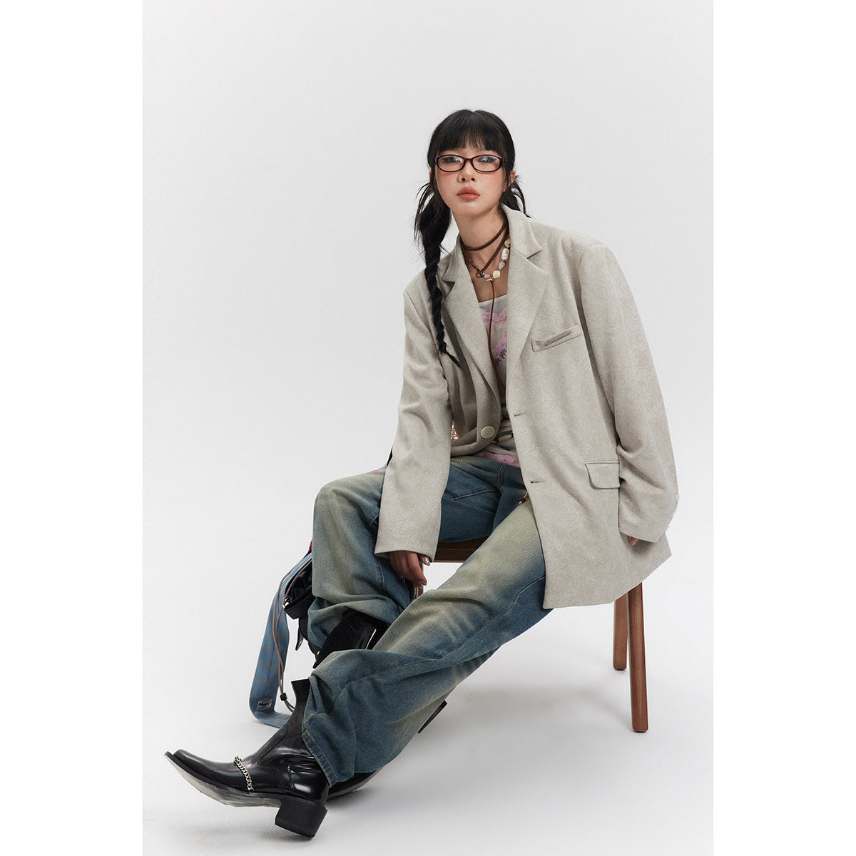Seated model wearing an oversized light beige patterned blazer with jeans.