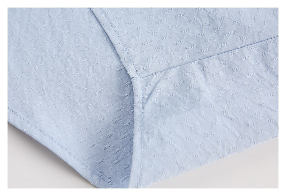 Close-up of pale blue shirt fabric showing a stitched seam and overlapping panels.