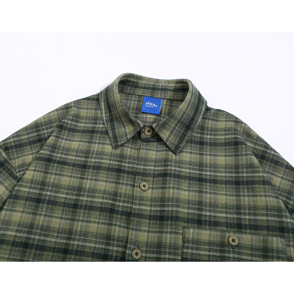 Close-up of an olive and charcoal plaid shirt front, showing the collar, buttons, chest pocket, and blue neck label.