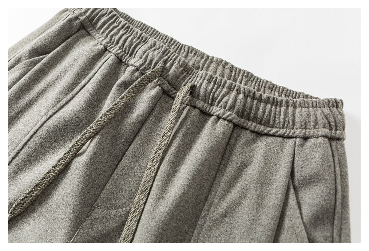 Close-up of light gray pants with an elastic waistband, braided drawstrings, and a front pocket.