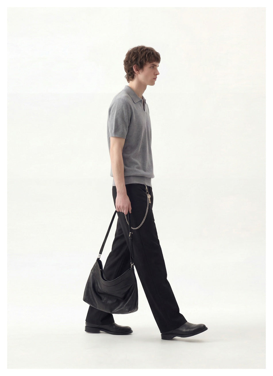 Side view of a model wearing a gray short-sleeve collared polo and loose black trousers, carrying a black bag.