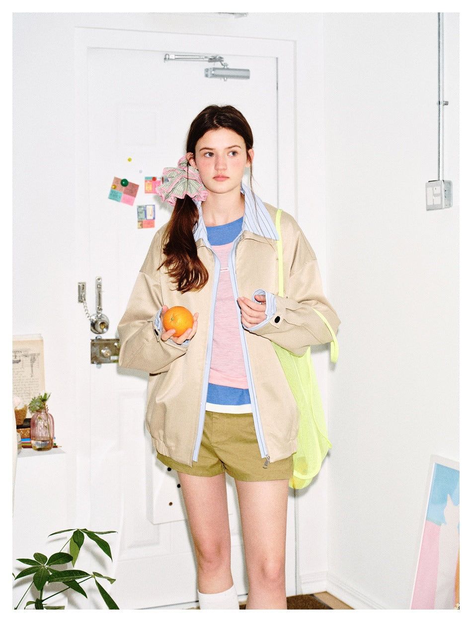 Model wearing an open beige jacket with a blue striped collar and cuffs, paired with olive shorts.