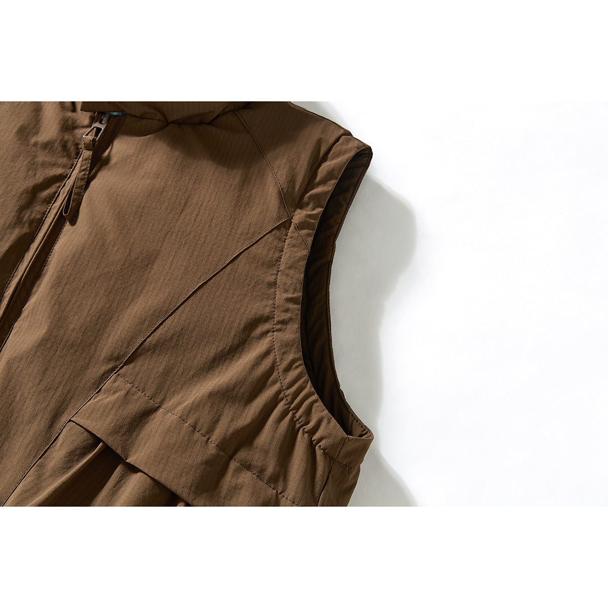 Close-up of a brown vest's shoulder, armhole, and curved front seam.
