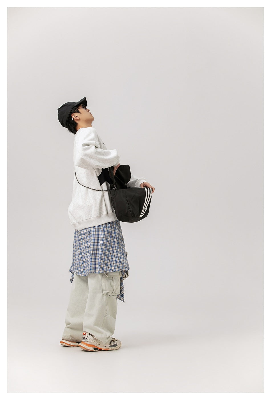 Side view of a model wearing a light gray sweatshirt with black panels, carrying a black bag.