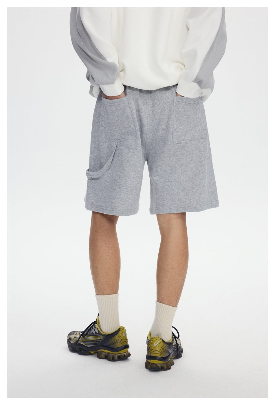 Rear view of a model wearing light gray shorts with two large patch pockets and a side utility loop.