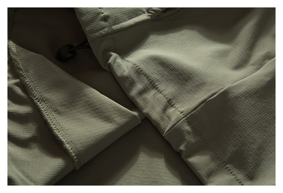 Close-up of olive khaki garment panels, stitching, and a black drawcord toggle.