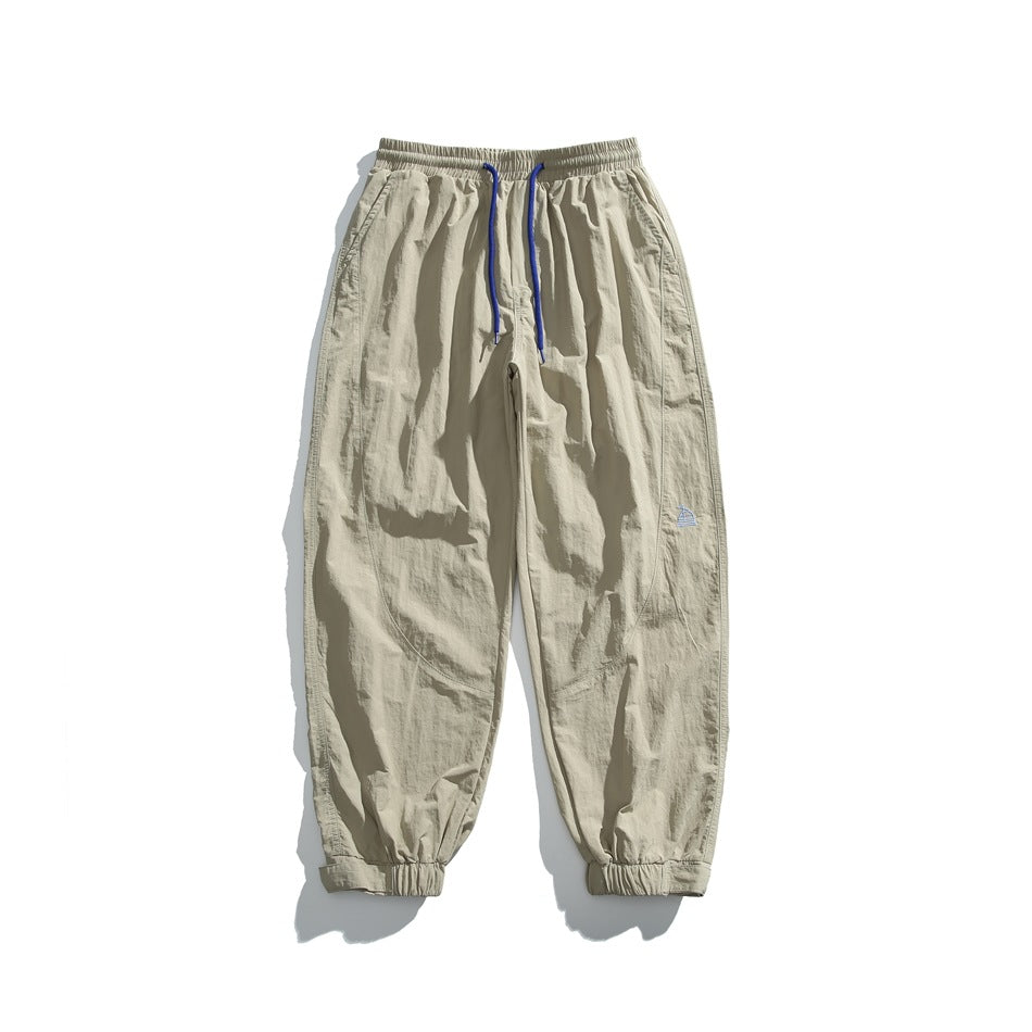 Khaki jogger-style pants with blue drawstrings, elastic cuffs and a small embroidered motif, laid flat