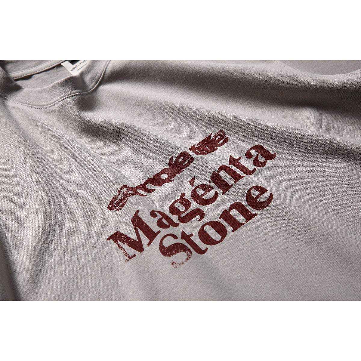 Close-up of a light taupe T-shirt with distressed dark red lettering printed across the chest.