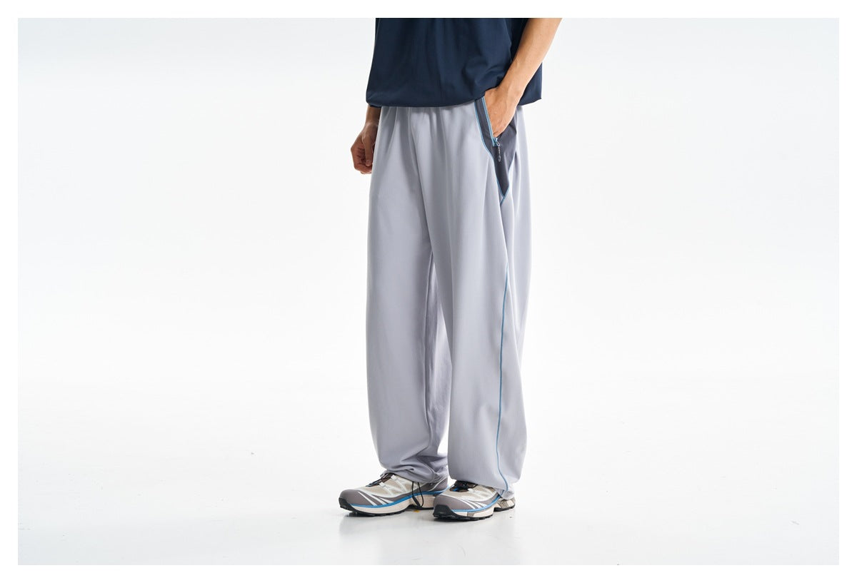 Front view of a model wearing loose light gray pants with blue side piping and a zippered pocket.