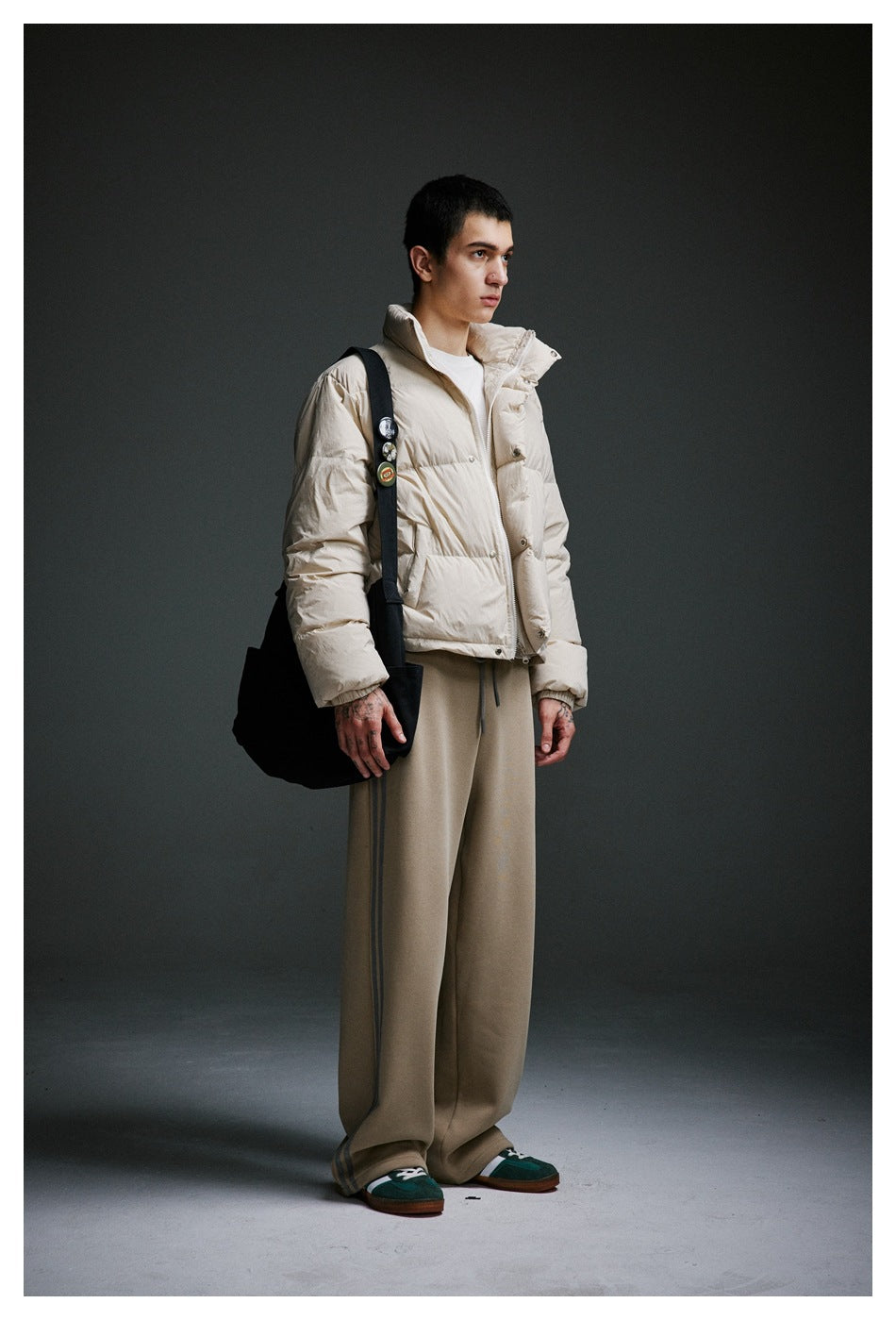 Side view of a model in a cream puffer jacket and wide-leg taupe pants with gray side stripes.