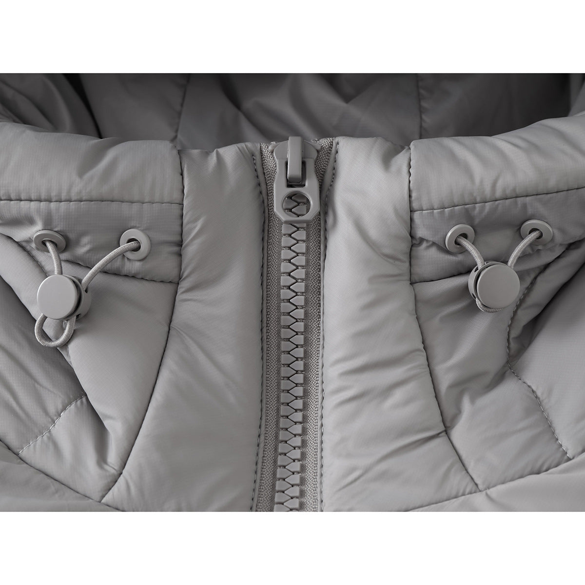 Close-up of the light gray jacket's chunky front zipper and paired hood drawcord toggles.