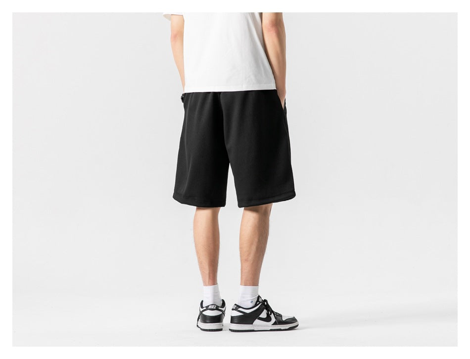 Rear view of a model wearing plain black knee-length shorts.
