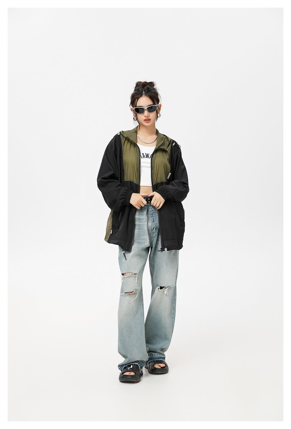 Front view of a model wearing an open black and olive hooded jacket with light distressed jeans.