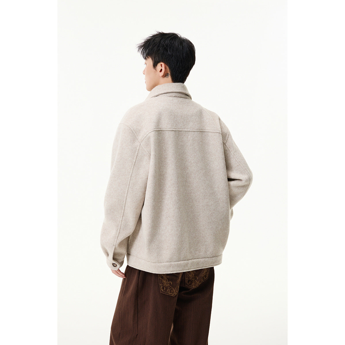Back view of a person wearing a light beige-gray collared jacket with long sleeves and buttoned cuffs.