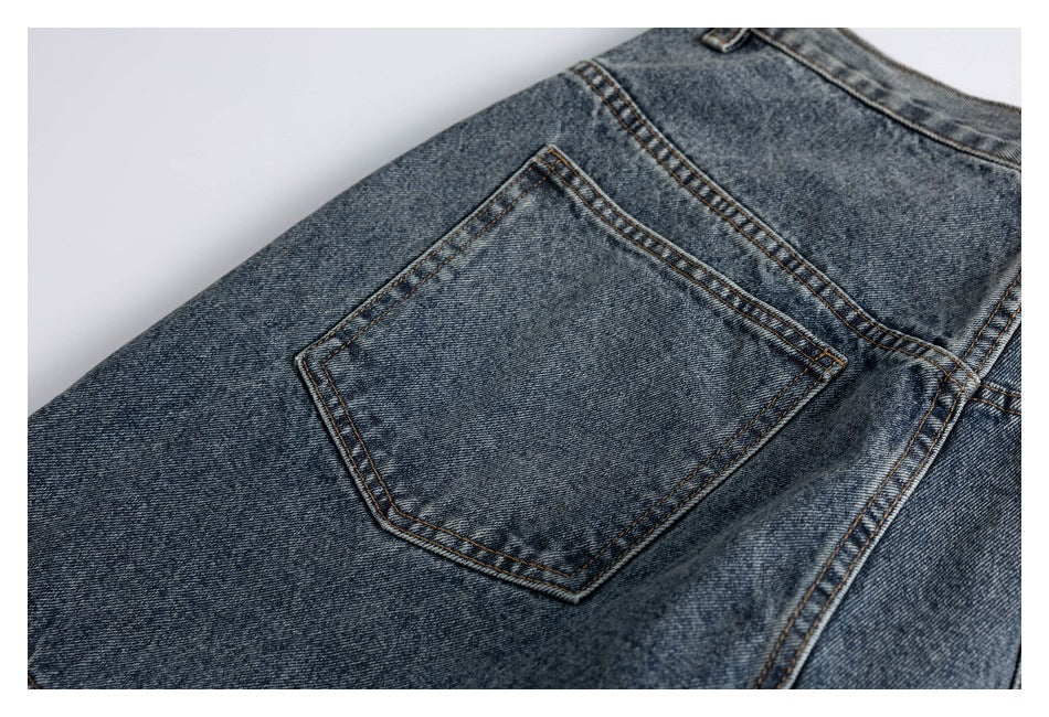 Angled close-up of a back patch pocket and contrast stitching on blue-gray jeans.