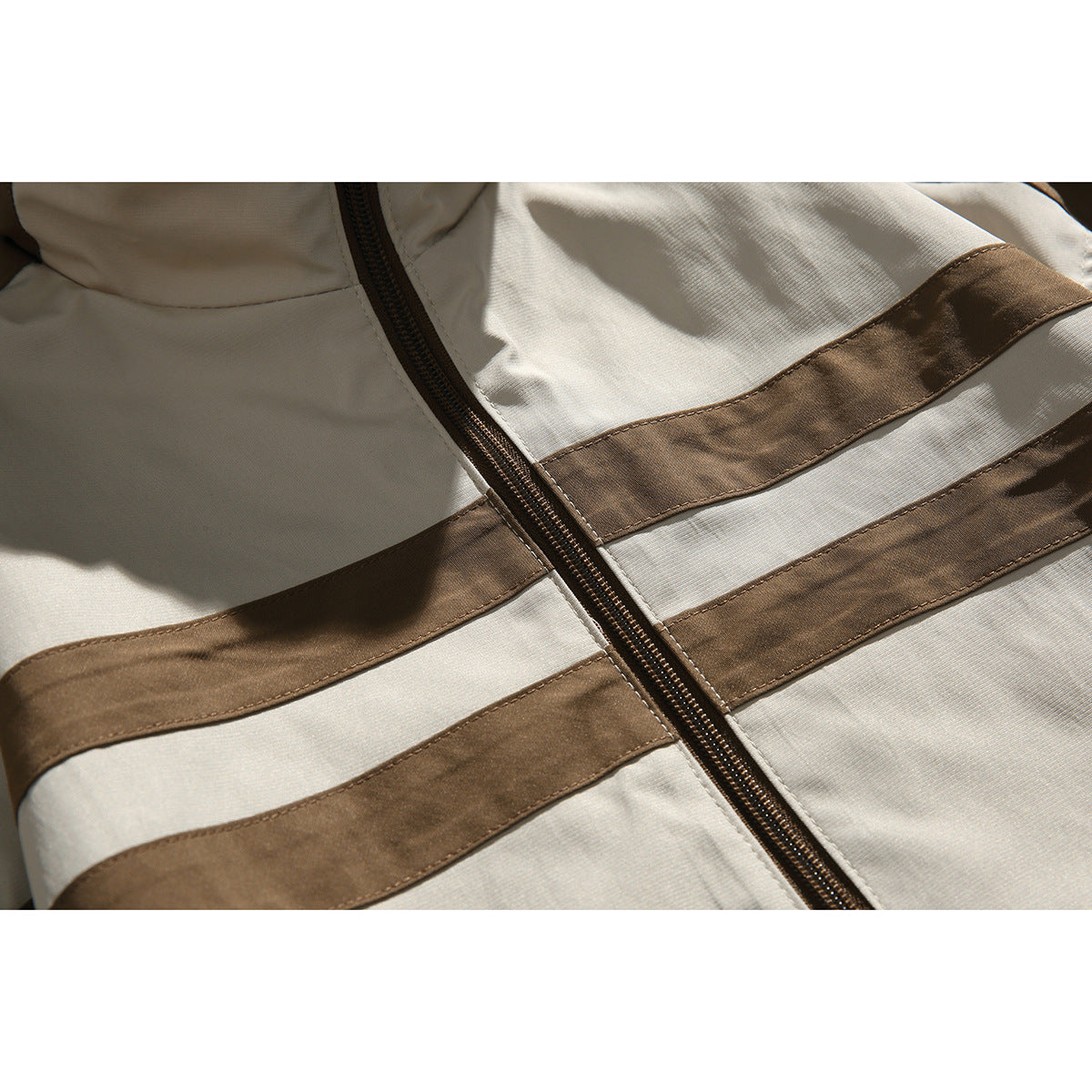 Close-up of a cream and brown jacket's front zipper and horizontal chest stripes.
