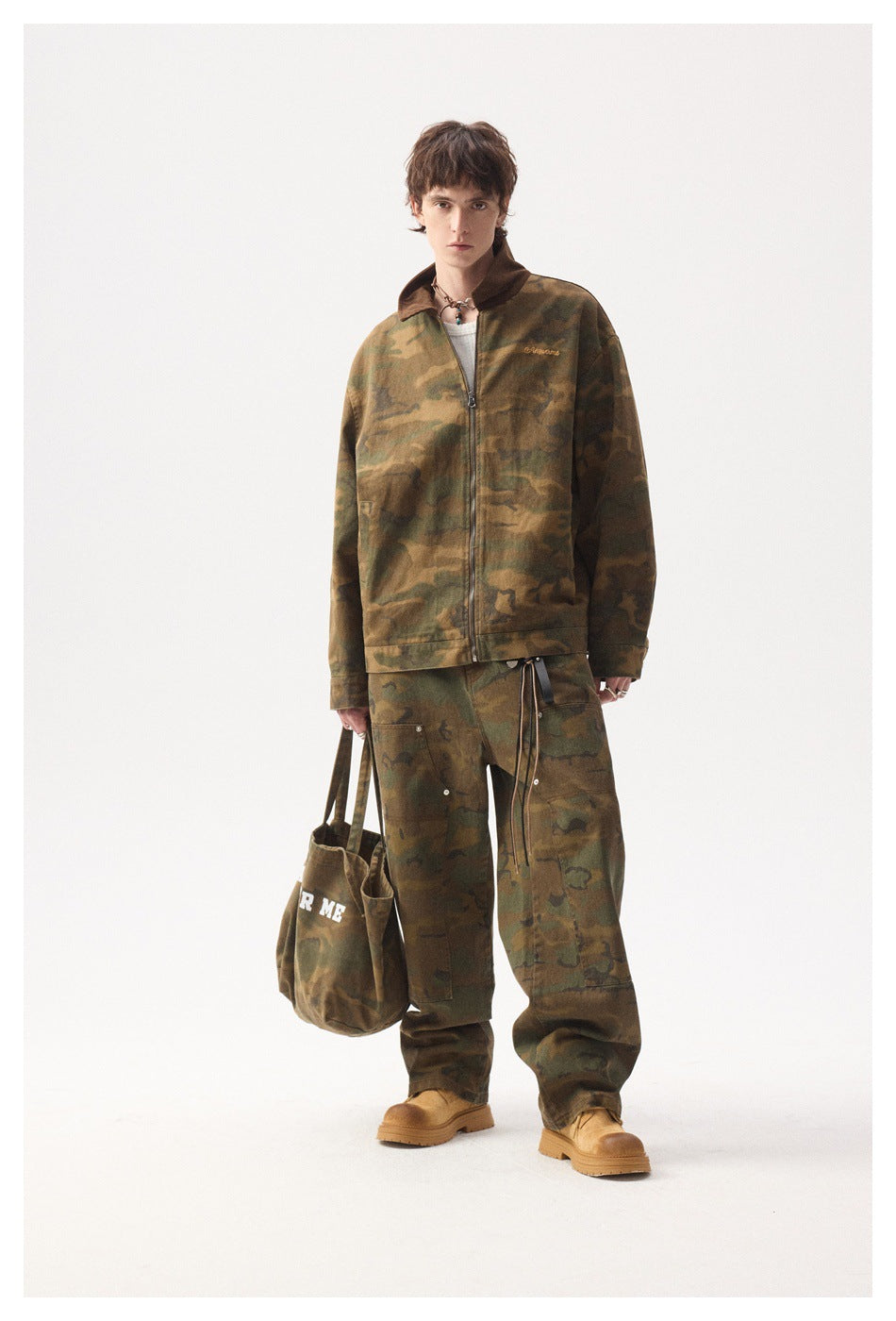 Full-length front view of a model wearing a camouflage zip jacket and loose matching trousers with tan boots.