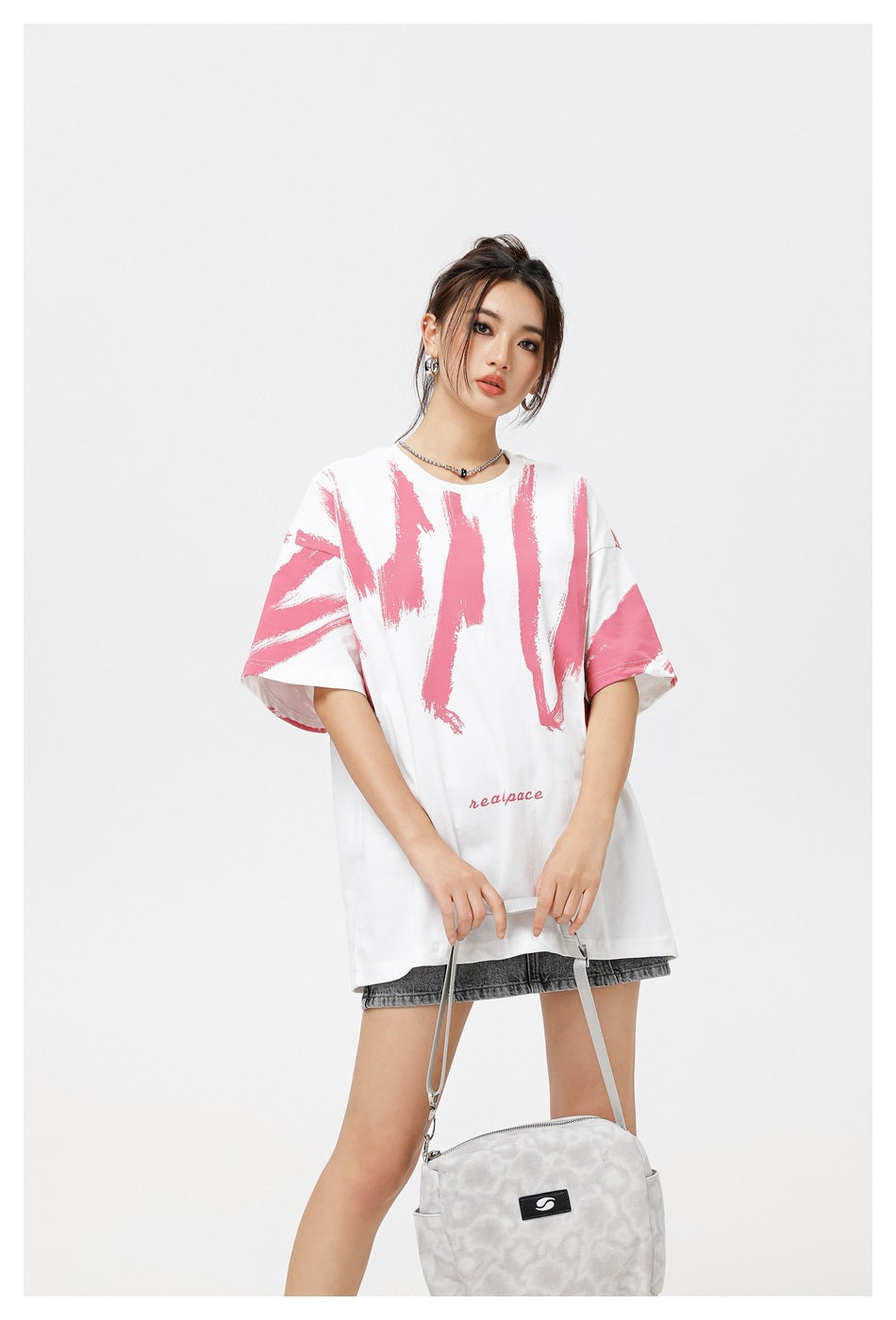 Model wearing an oversized white T-shirt with pink brushstroke graphics and small pink lettering, shown from the front.