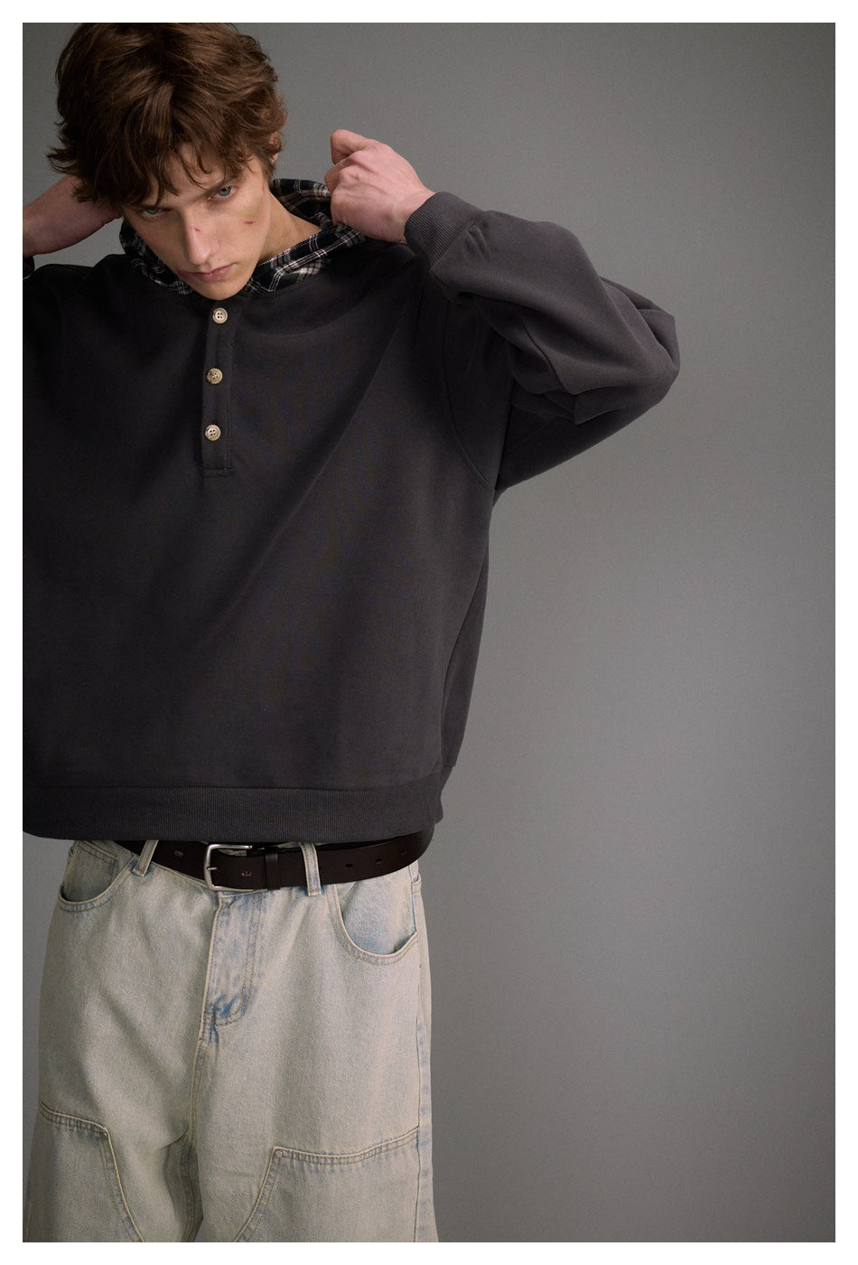 Front view of a model wearing a charcoal pullover hoodie with a plaid-lined hood and three-button placket.