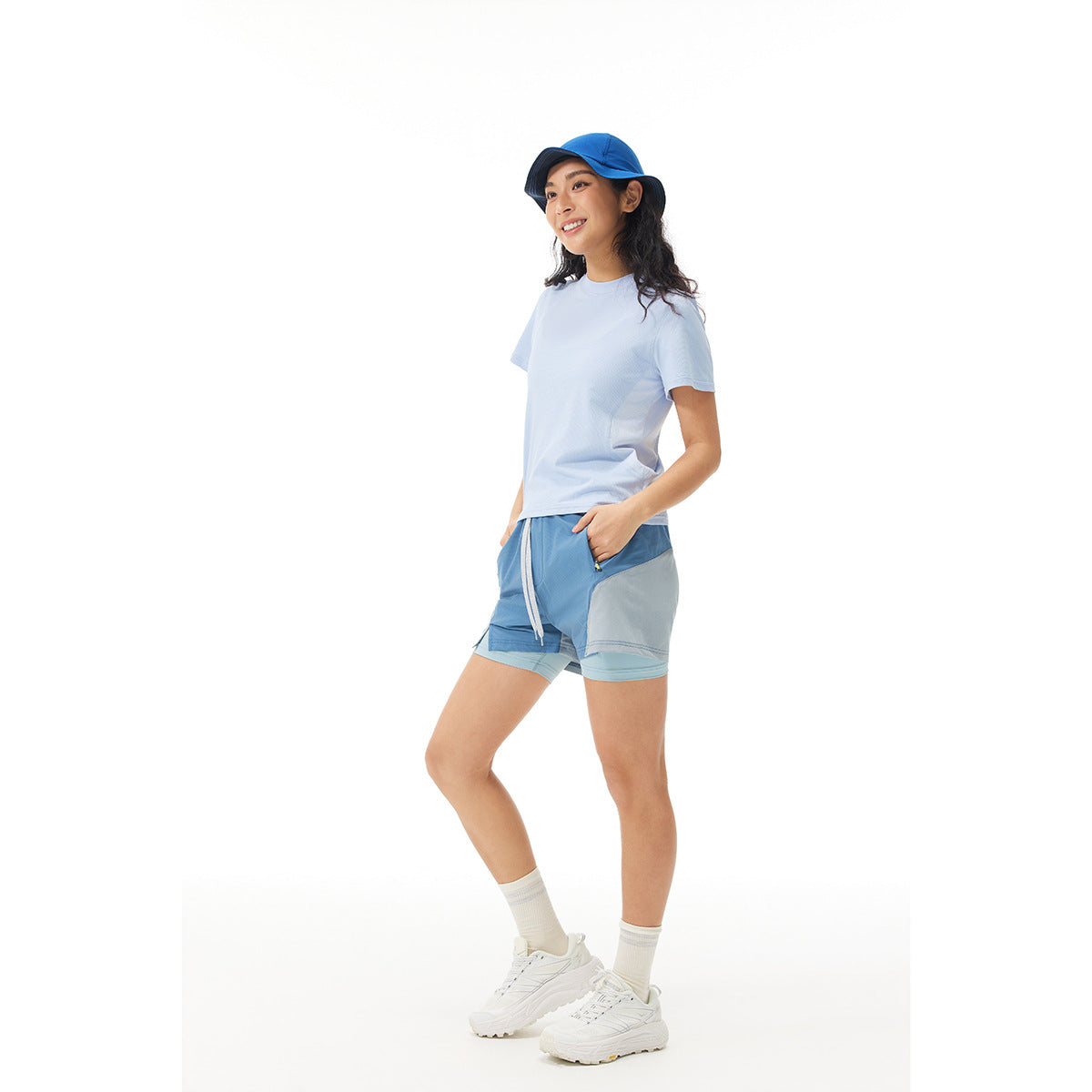 Model wears a pale blue T-shirt and blue layered athletic shorts with a blue cap against a white background.