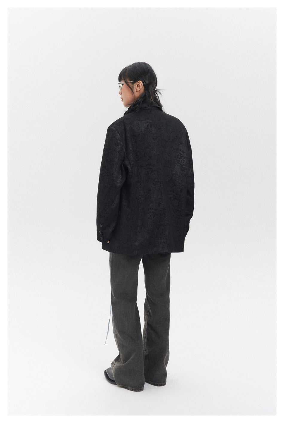 Rear view of a model wearing a black tonal-pattern blazer and dark wide-leg jeans.