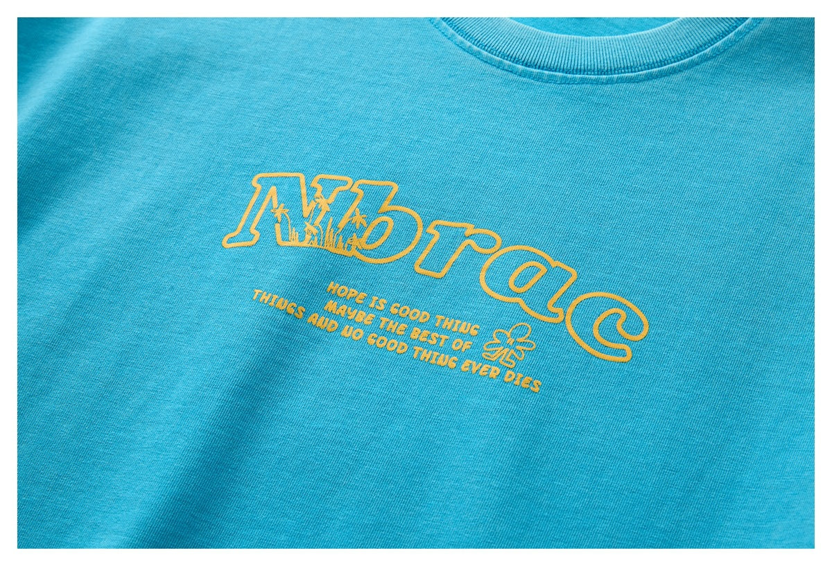 Close-up of yellow outlined lettering and small text printed on the front of a turquoise T-shirt.