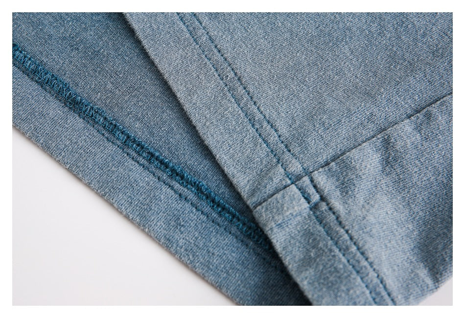 Close-up of blue-gray knit fabric showing an overlocked edge and intersecting stitched seams.