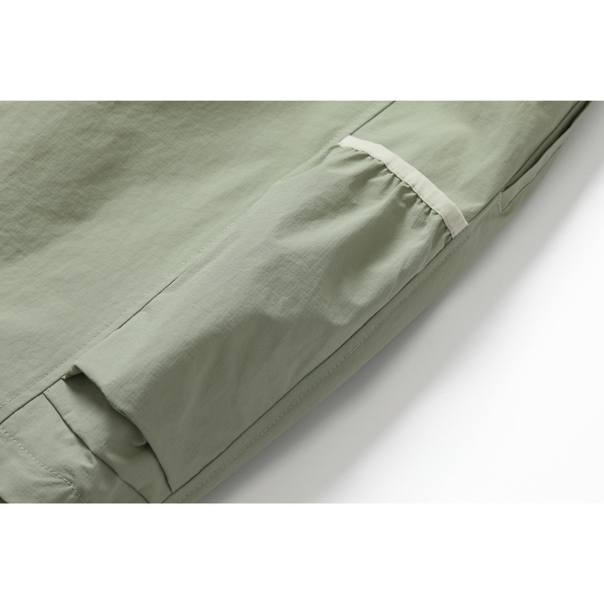 Close-up of pale sage-green pants showing a flap cargo pocket and contrast trim.