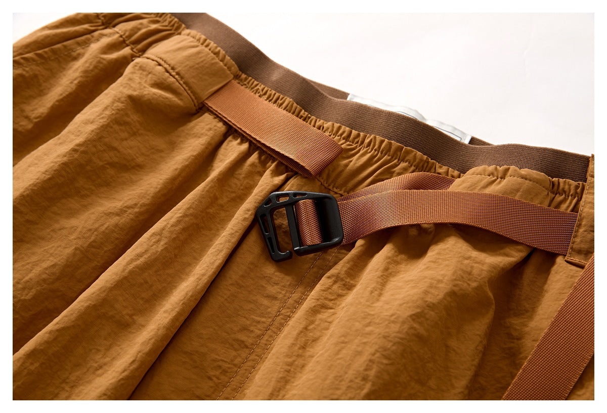 Close-up of rust-brown shorts with an adjustable webbing belt and black buckle across the gathered waistband.