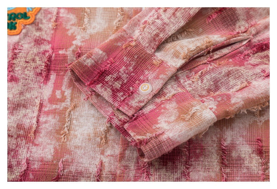 Close-up of a buttoned shirt cuff against distressed pink, cream and tan plaid fabric.