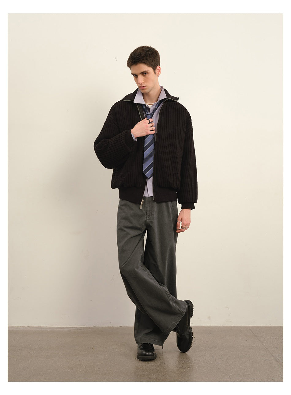 Model wearing a black ribbed zip jacket over a lavender shirt and striped tie with wide charcoal trousers.