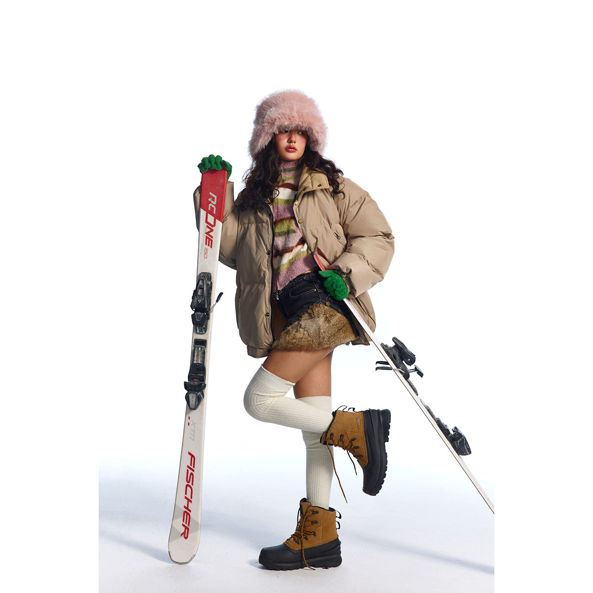 Model wearing a beige oversized puffer jacket with a high collar, posed with skis against a white background.