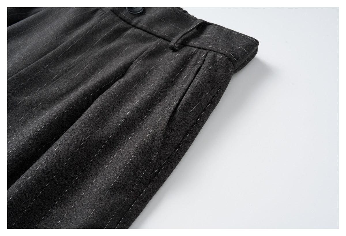 Close-up of charcoal pinstripe trousers showing the waistband, belt loop, button, and front pleats.
