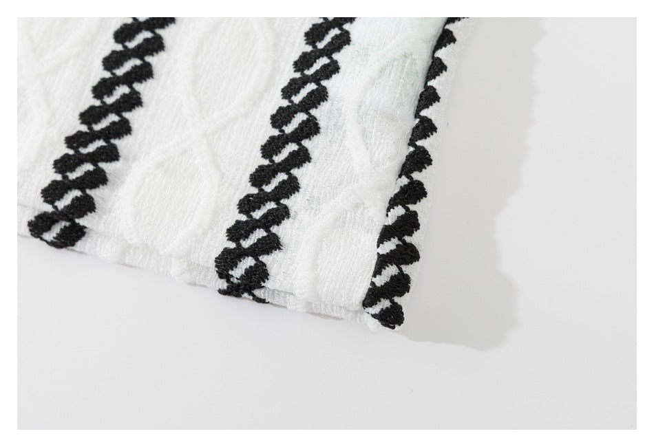 Close-up of the garment's white hem edge, bordered by black embroidery against a light background.