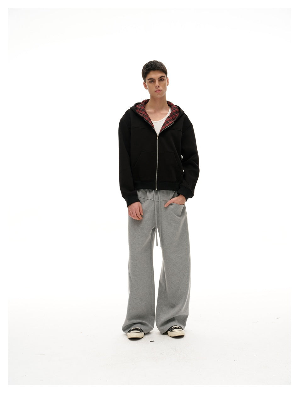 Front view of a model wearing a black zip-up hoodie with red plaid lining and loose gray drawstring pants.