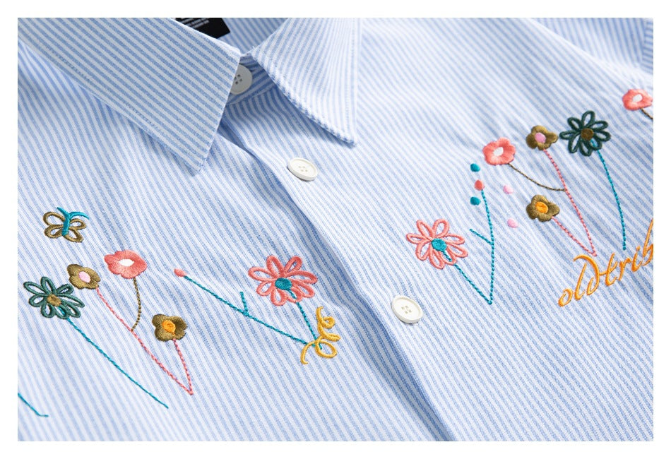 Close-up of a blue-and-white striped shirt with colorful embroidered flowers and cursive lettering.