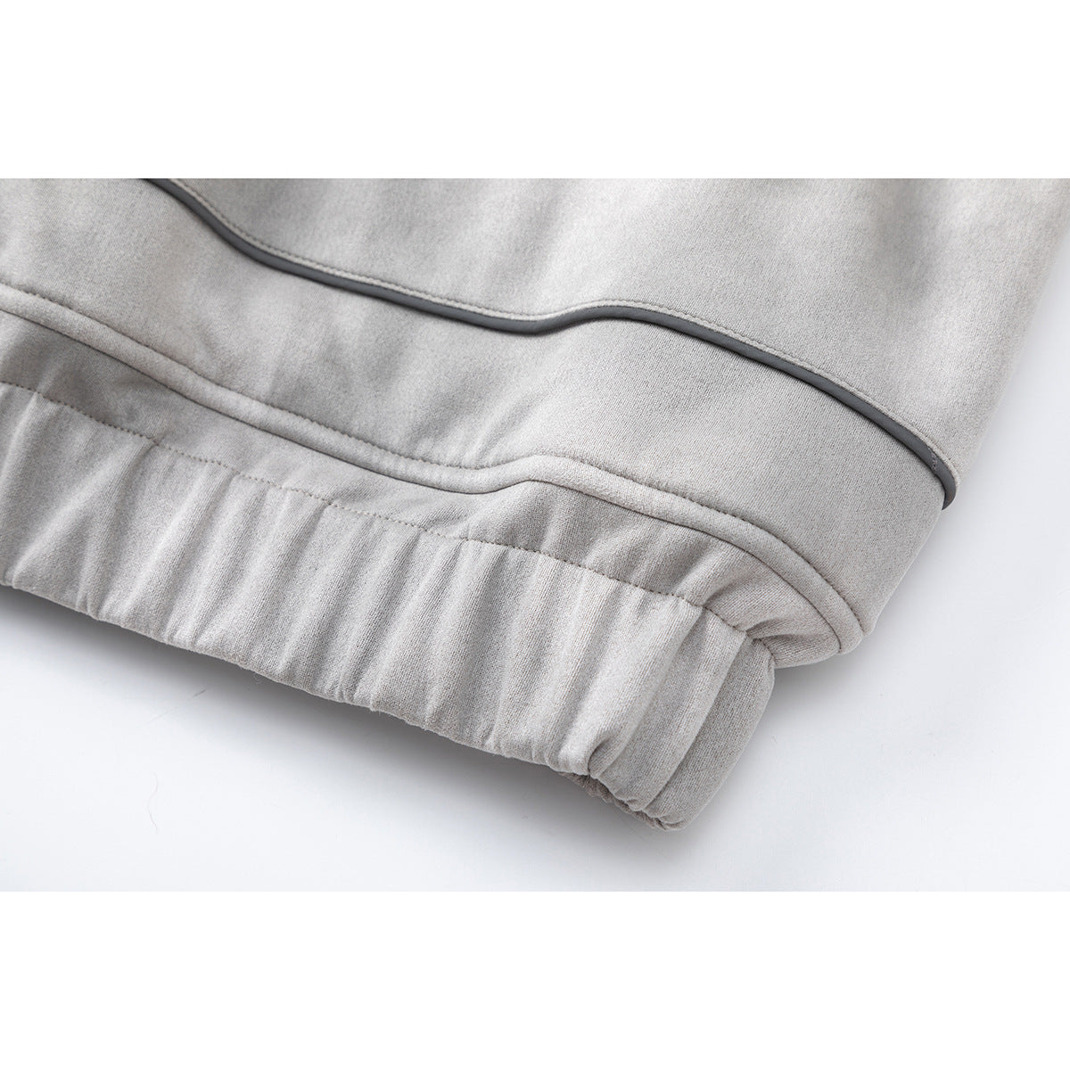 Close-up of a light gray coat's gathered elastic hem and dark piping.