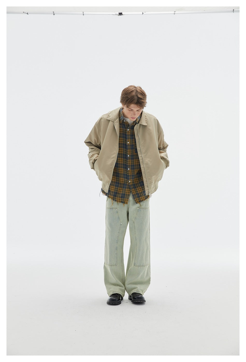 Front view of a model in a beige zip-front jacket over a plaid shirt and pale green wide-leg jeans.