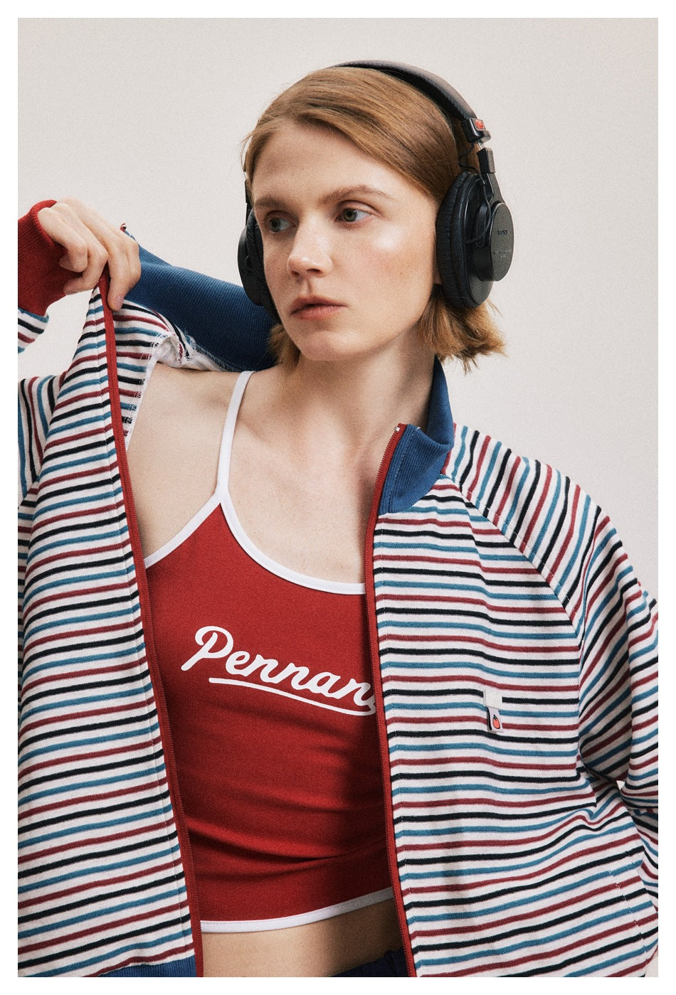 Close-up of an open striped jacket showing a red cropped top with white script and the jacket's blue collar and red zipper.