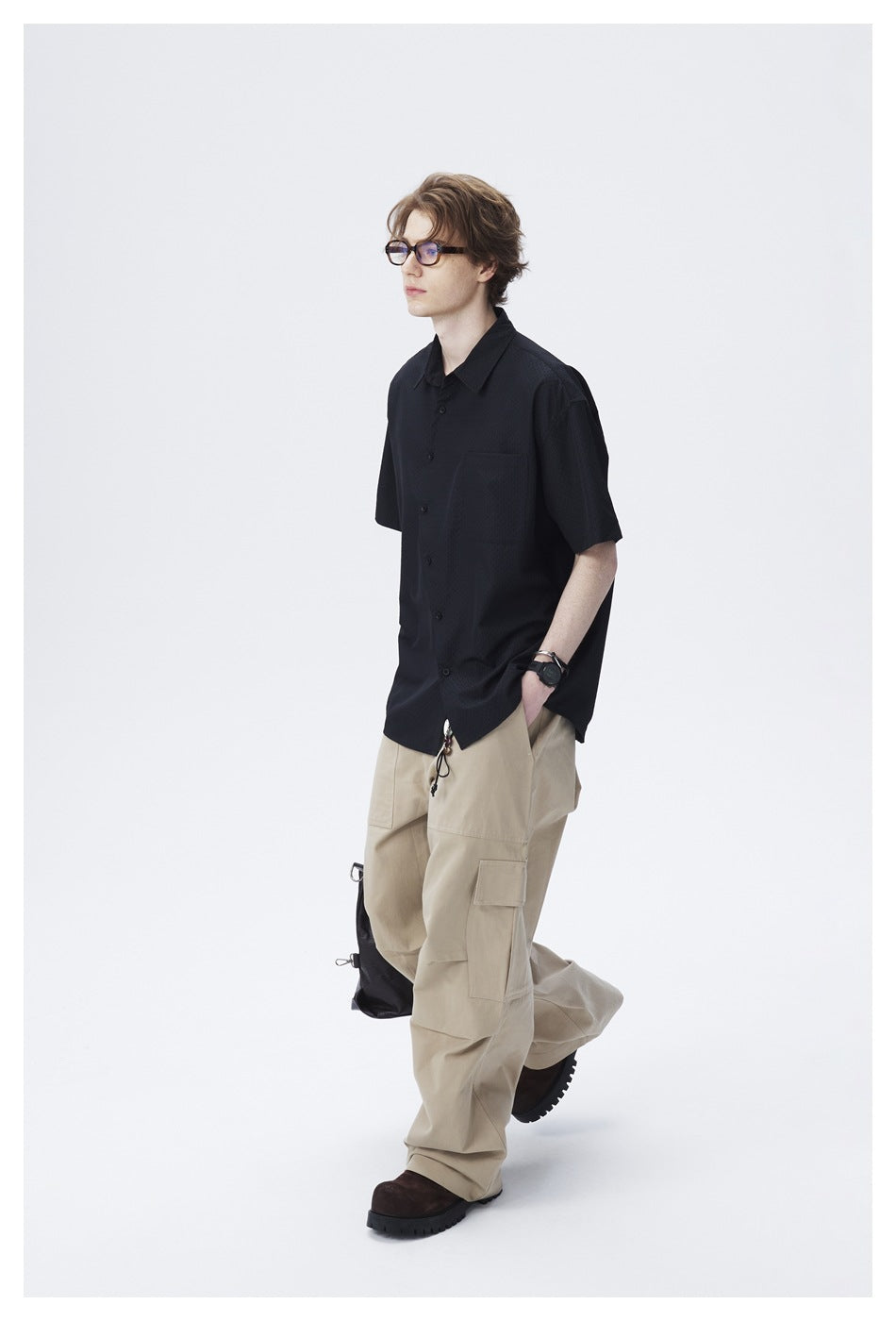 Full-length view of a model in a black short-sleeve shirt and loose beige cargo trousers.