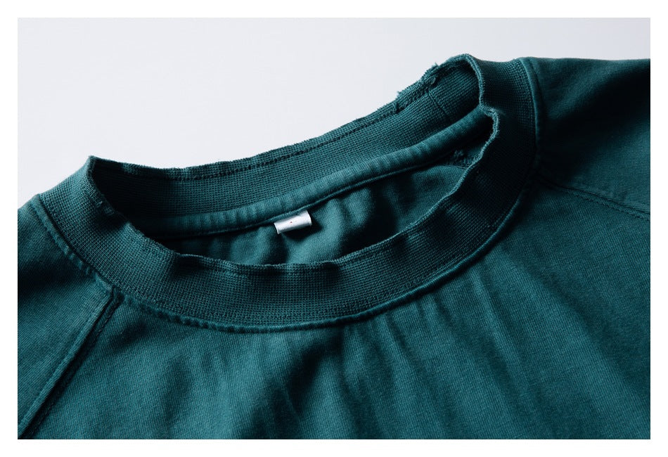 Close-up of the deep teal top's ribbed crew neckline, inner neck seam, and raglan shoulder stitching.
