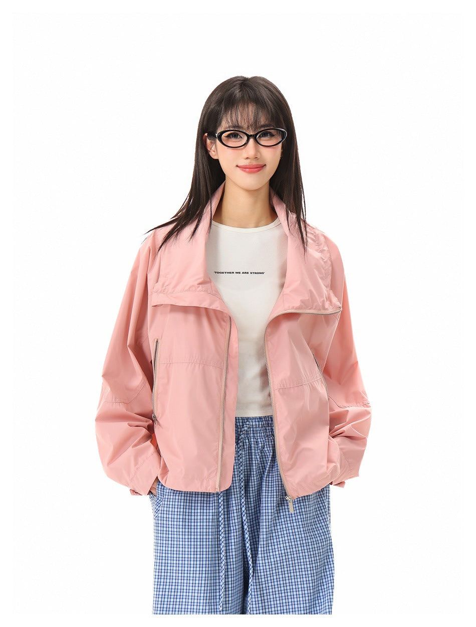 Close view of model wearing pink zip jacket with folded collar over a white graphic tee and blue gingham pants