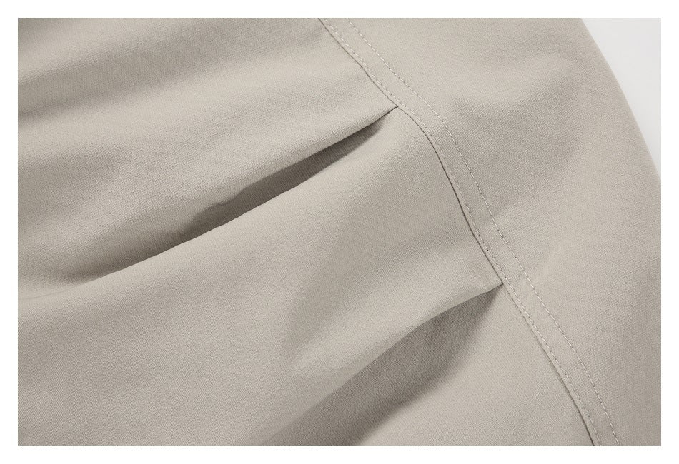 Close-up of beige garment fabric with folded sections and a curved double-stitched seam.